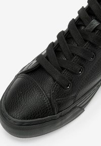 Basket en cuir noir avec surface texturée, bout rond et œillets en métal. Dotée de lacets plats noirs et d'une semelle en caoutchouc avec un motif de semelle.