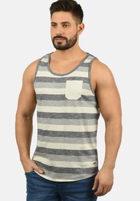 Stribet grå og creme tanktop med rund hals, der har en frontlomme og en lige kant. Lavet af letvægtsstof.
