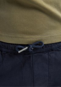 T-shirt vert olive avec un ourlet droit, associé à un pantalon à taille élastique bleu marine avec un cordon de serrage bleu et un stoppeur argenté.