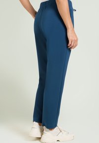 Blaue Sweatpants mit einem lässigen Schnitt, elastischem Bund und seitlichen Taschen. Kombiniert mit weißen Sneakers mit strukturiertem Design.