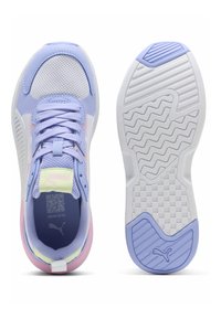 Zapatilla Puma en tonos lila claro y blanco que muestra la parte superior con cordones y la suela con surcos estampados y detalles en morado.