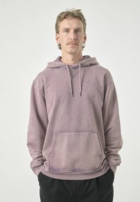 Lila Kapuzenpullover aus weichem Material, mit einer Vordertasche, Zugbandkapuze und einem dezenten Logodetail auf der Brust.