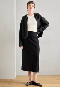 Czarna midi spódnica połączona z białą prążkowaną bluzką, nałożoną pod ciemnoszary krótki kardigan. Czarne buty wsuwane z srebrnymi akcentami.