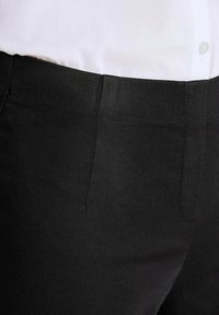 Zwarte broek met een gladde textuur, voorzien van een klassiek recht model en zijzakken. Close-up weergave benadrukt de stof en de naden.