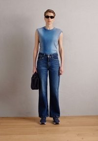 Haut sans manches bleu à côtes, jeans en denim noir taille haute, lunettes de soleil noires et sac à main noir texturé, associés à des baskets sombres.