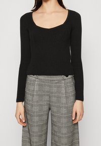 Svart, ribbad långärmad topp med rundad halsringning, kombinerad med högmidjade, rutiga vida byxor i svarta och grå nyanser.