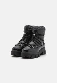 Black, puffy ankle boots with a glossy finish, featuring lacing and silver hardware; thick, rugged soles with distinct tread pattern.