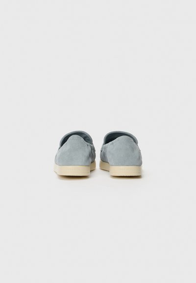 Scarpe slip-on in suede azzurro chiaro con punta rotonda e suola in gomma beige. Presentano una texture liscia e un design minimalista.
