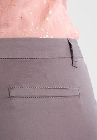 Šedé bavlněné kalhoty s elegantním designem, které mají nenápadnou zadní kapsu a kontrastní švy. Materiál vypadá hladce a jemně.