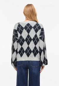 Pull à motifs argyle gris et marine, coupe décontractée avec des manches larges, en tissu tricoté texturé.