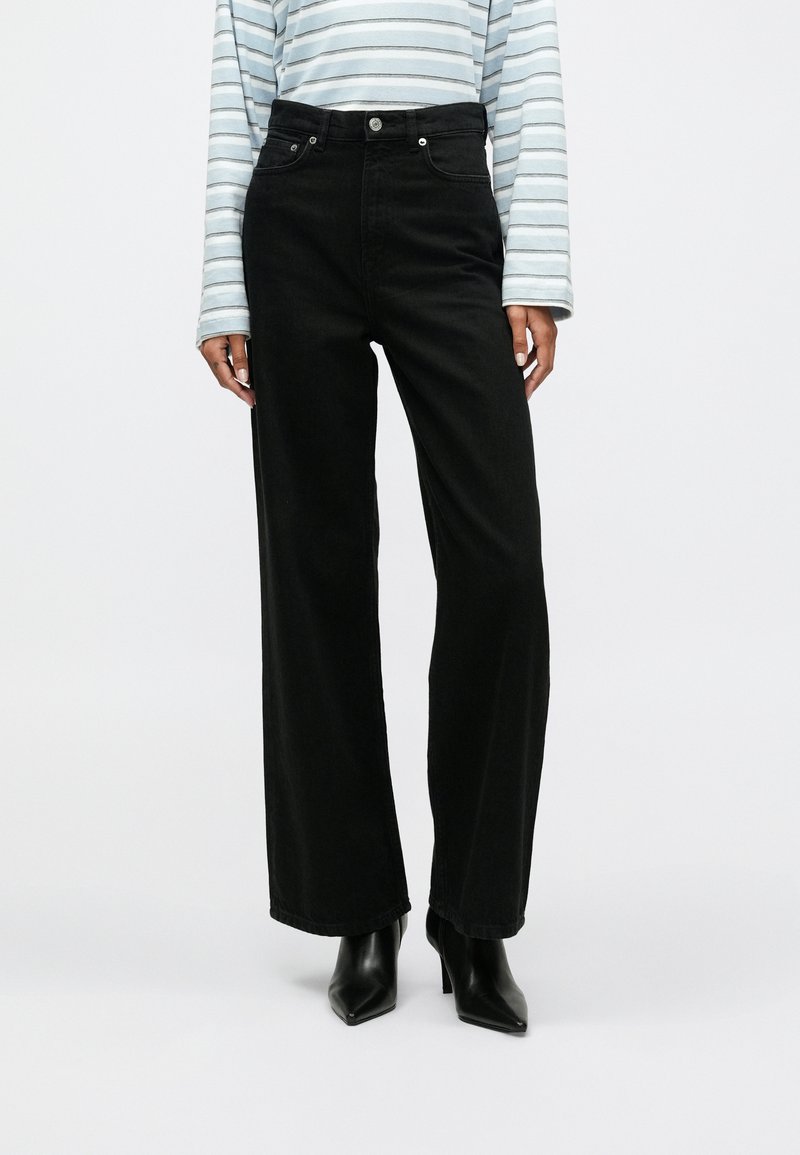 Μαύρα τζιν παντελόνια σε φαρδιά γραμμή, κατασκευασμένα από τζιν με ψηλή μέση. Διαθέτουν μπροστινές τσέπες και κλείσιμο με κουμπί. Συνδυάζονται με μπλε μπλούζα με ρίγες.