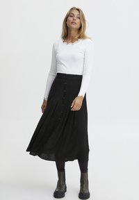 Hvid langærmet top med en bølget halsudskæring, parret med en sort midi-nederdel med frontknapper og let stof. Kraftige sorte støvler.