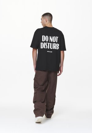 Black t-shirt with "DO NOT DISTURB" in large white text on the back, paired with brown cargo pants and white sneakers.