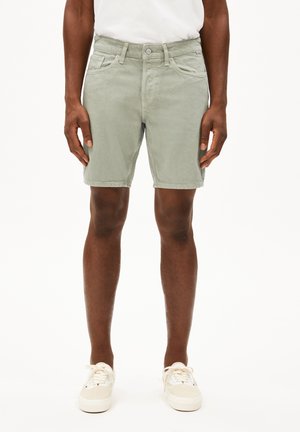 Shorts di denim verde chiaro con vestibilità dritta, tasche frontali e chiusura con bottone, abbinati a sneakers crema e una t-shirt bianca.