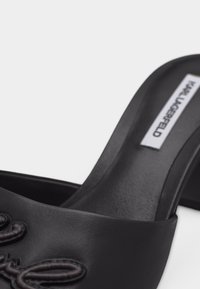 Κοντινή λήψη μαύρου δερμάτινου παπουτσιού χωρίς κορδόνια με κεντημένη λεπτομέρεια και εμφανές ένθετο με το όνομα της μάρκας στο εσωτερικό.