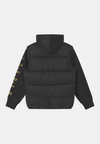 Sort puffer vest med hætte, der har en quiltet tekstur og lange ærmer. Guldtekst på ærmet tilføjer detaljer til designet.