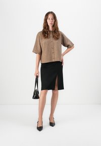 Brun ullblanding kortermet cardigan med knapper, parret med en svart kne-lengde skjørt med en frontsplitt. Svart spiss tå hæler.