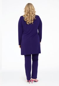 Lilla tunika og matchende bukser lavet af blødt stof. Lange ærmer og lige snitdesign. Klart pink højhælede sandaler.