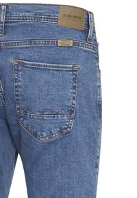 Jeans in denim blu medio con una finitura testurizzata, dotati di una tasca posteriore con pattina e dettagli cuciti. Etichetta del marchio in vita.