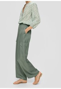 Ljusgrön blus med geometriskt vitt mönster, ihop med lösa mörkgröna satinklänningar med sidofickor. Platta sandaler fulländar looken.