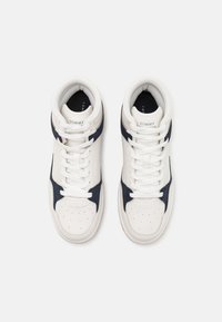 Fehér bőr magas szárú tornacipő, tengerészkék kiegészítésekkel. Lyukacsos orral, lapos fűzőkkel és gumitalppal rendelkezik. "TOMMY" logó a nyelvén.