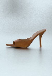 Mule en cuir marron à bout ouvert avec talon aiguille fin sur une surface réfléchissante gris clair et en arrière-plan.
