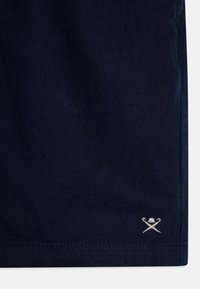 Tessuto blu navy con una superficie liscia, caratterizzato da un piccolo logo ricamato bianco vicino all'orlo. Design sartoriale con bordi puliti.