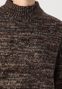 Gestrickter Pullover mit hohem Kragen, grober Struktur und einem mehrfarbigen Braunton mit Einsprengseln aus helleren und dunkleren Fäden.