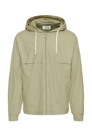 Veste coupe-vent beige clair zippée avec capuche, cordons blancs, deux poches avant et poignets élastiques.
