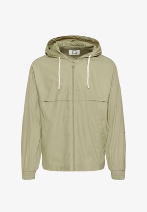 Veste coupe-vent beige clair zippée avec capuche, cordons blancs, deux poches avant et poignets élastiques.