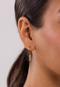 Goldene Creolen mit einem vertikalen rechteckigen Bar-Pendant, glatt poliert mit einem glänzenden Finish, die am Ohrläppchen getragen werden.