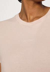 Light pink cotton t-shirt with a round neckline and short sleeves featuring a subtle, embossed "Calvin Klein" logo on the front.