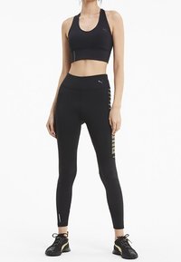 Czarny sportowy top crop i legginsy wykonane z elastycznego materiału, z logo i bocznymi akcentami, w połączeniu z czarnymi butami sportowymi.