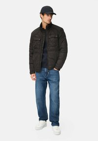 Sort quiltet pufferjakke med høj krave, der har to brystlommer; samt mørkeblå jeans og hvide sneakers.