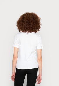 Vit bomull t-shirt med korta ärmar, rund halsringning och en slät textur. Buren med svarta texturerade tights. Bakifrån visar den en enkel design.