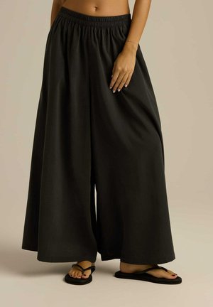 Czarne spodnie typu wide-leg wykonane z zwiewnego materiału z elastycznym pasem, o gładkiej fakturze i minimalistycznym designie.