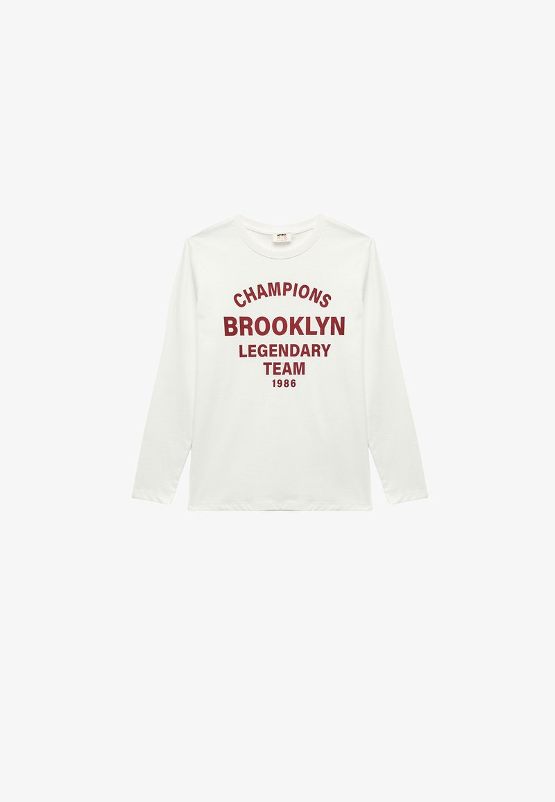 Biała koszulka z długim rękawem wykonana z bawełny, z czerwonym napisem: "CHAMPIONS BROOKLYN LEGENDARY TEAM 1986" w pogrubionym, łukowatym wzorze.