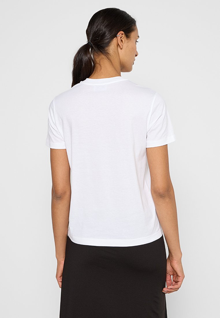 Biała koszulka z krótkim rękawem, okrągłym dekoltem, wykonana z miękkiej bawełny, z prostym dołem i minimalnymi szwami, noszona z czarną spódnicą.