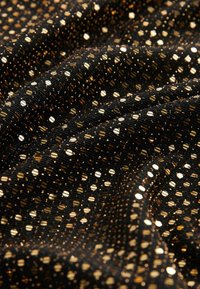 Czarna tkanina z błyszczącymi złotymi metalicznymi groszkami, pokazana z bliska z miękkimi fałdami i teksturowanym prążkowaniem.