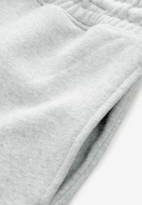Hellgraue Jogginghose aus weichem Stoff, mit elastischem Bund und seitlichen Taschen, einer glatten Textur und dezenten Nähdetails.