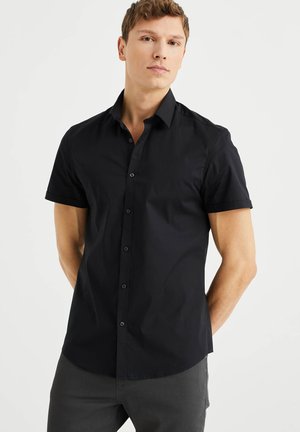 Short-sleeve, button-up shirt in black cotton fabric with a spread collar and straight hem. Features black buttons and rolled cuffs.