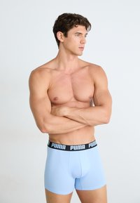 Boxeri clasici de culoare albastru deschis, cu un brad negru PUMA, având un design ajustat. Material neted și lungime până la mijlocul coapsei, fără modele vizibile.