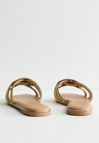 Sandales ouvertes à bout doré tressé avec une semelle plate beige et des fines lanières, mettant en avant un léger accent métallique le long du bord pour une touche de détail supplémentaire.