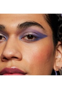 Nahaufnahme eines Gesichts mit lila Lidschatten im Verlauf, sanftem Rouge auf den Wangen und glanzfarbigem, gedämpftem Lippenstift. Die Hautstruktur ist sichtbar.