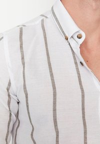 Valkoinen nappipaita, jossa ohuet, vaakasuorat harmaat raidat. Pehmeä, kevyt kangas, pystykaulus ja ruskeat napit.