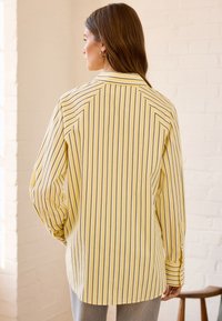 Camicia a righe gialle con maniche lunghe, caratterizzata da righe verticali blu navy, colletto classico e vestibilità comoda. Tessuto dalla texture liscia.