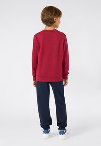 Sudadera roja de manga larga y cuello redondo, combinada con pantalones azul marino y zapatillas blancas y azules. Tela suave con un corte relajado.