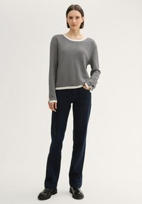 Schwarz-weiß kariertes Strickoberteil mit rundem Ausschnitt, kombiniert mit dunkelblauen schmal geschnittenen Hosen und schwarzen Stiefeletten.