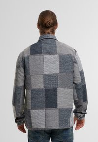 Gråternet skjorte med varierende nuancer af grå og blå. Har en klassisk krave og knapmanchetter. Vævet stofstruktur.