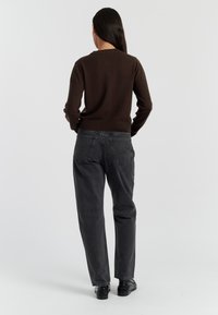 Bruin gebreid sweater met lange mouwen, gecombineerd met high-waisted, losse zwarte jeans en zwarte platte schoenen. Minimalistisch ontwerp, geen patronen.